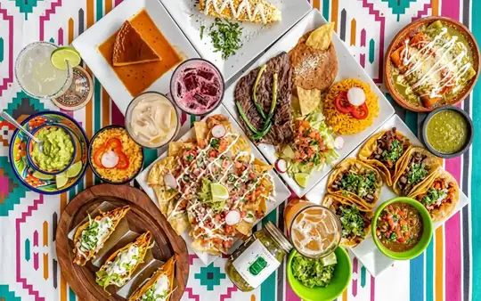Colorful spread of Viva Mexico dishes — tacos, guacamole, margaritas and enchiladas on a serape-patterned table